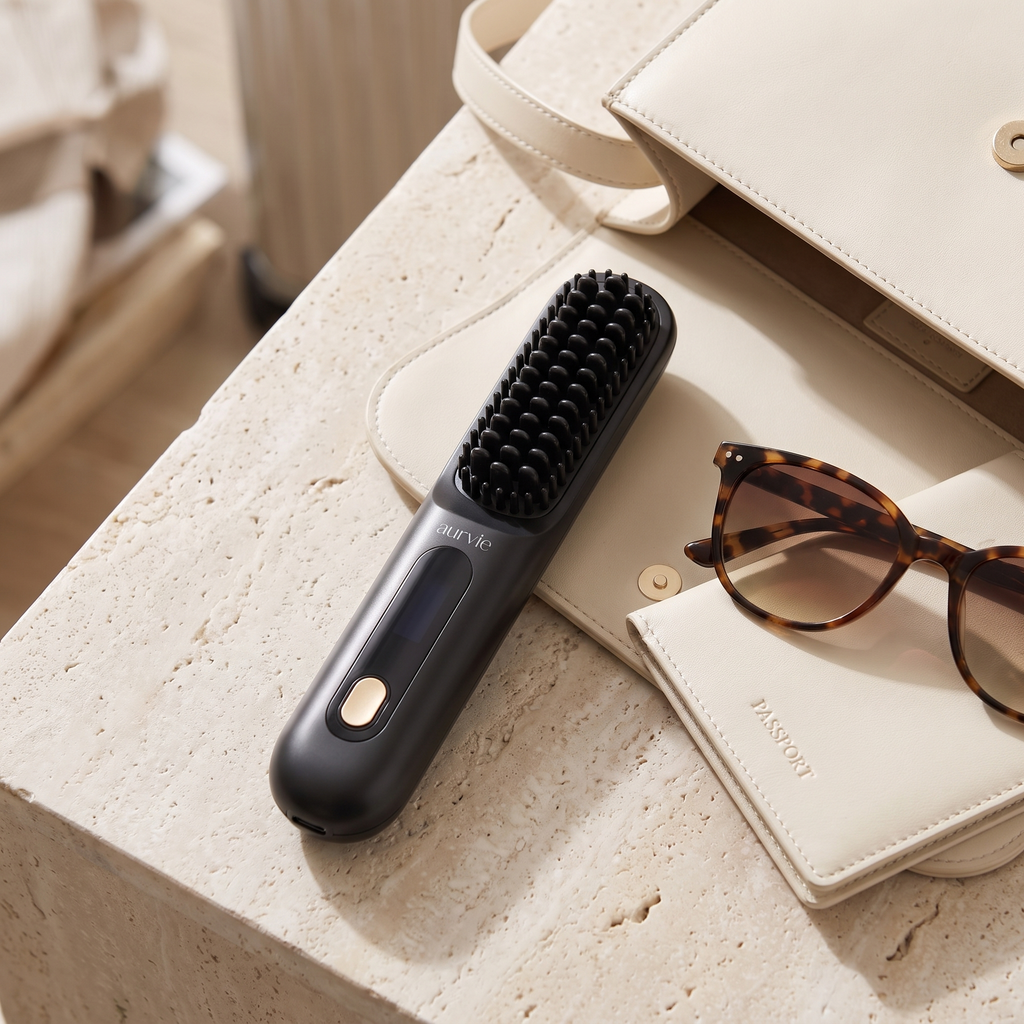 Straightening brush beside a handbag and sunglasses, packed for travel (ALT)